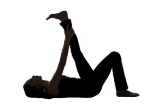 Silhouette of a woman performing a yoga stretching exercise on her back.